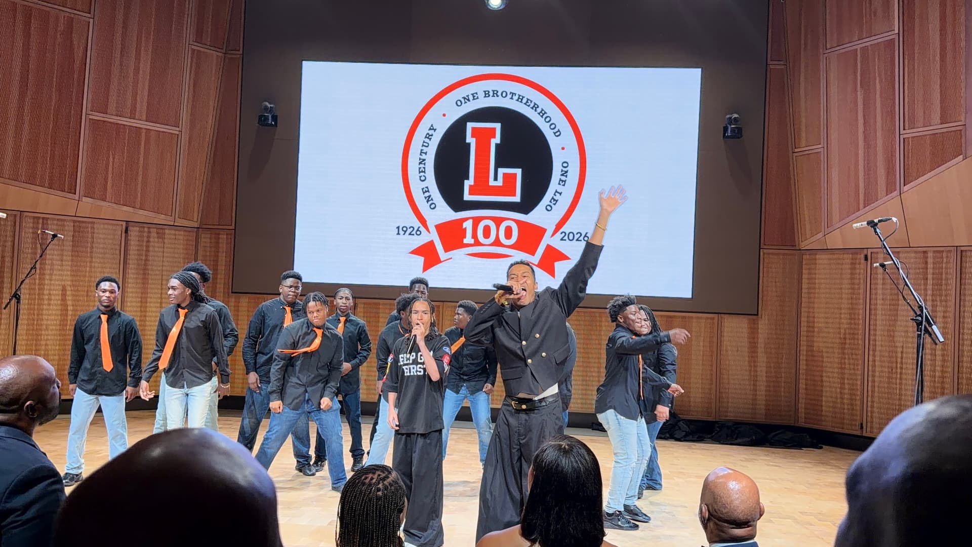 A guest vocalist with his arm raised, singing with the choir and a young performer