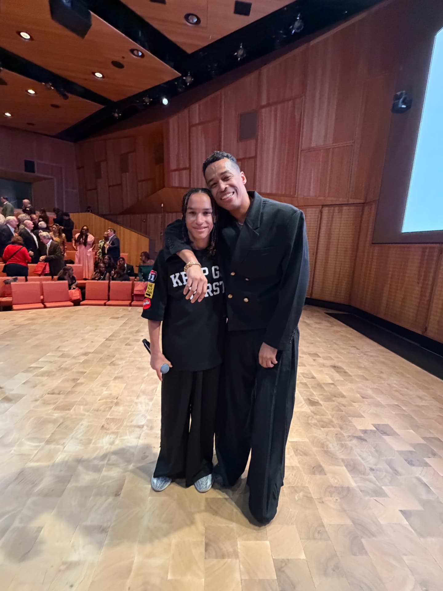 A young performer and a guest artist hugging on stage after the show