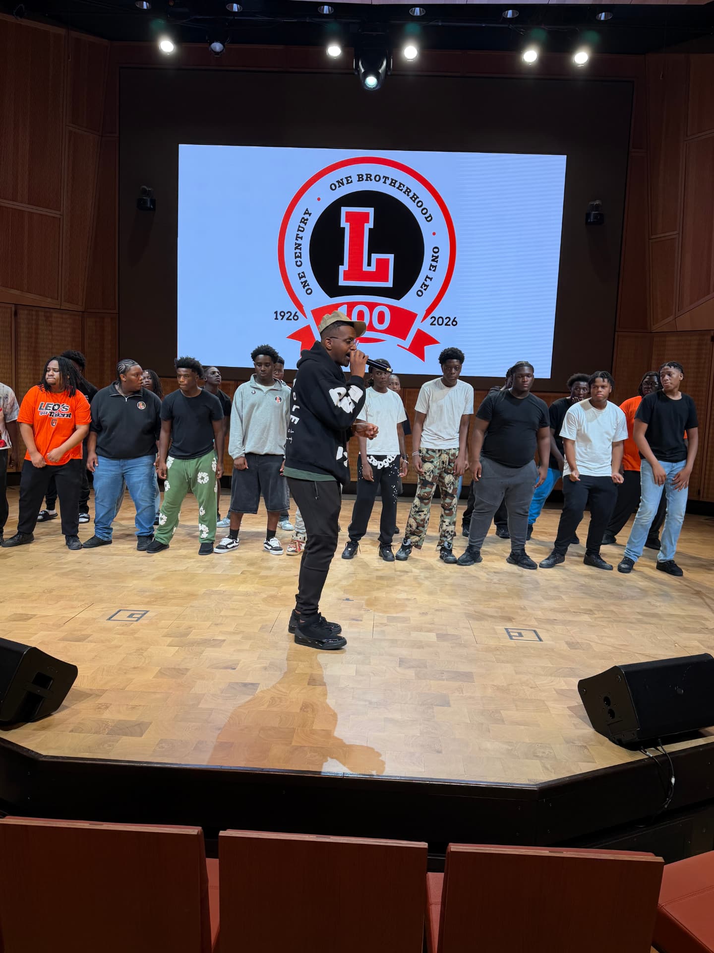 A guest vocalist rehearsing with the choir in front of the centennial crest