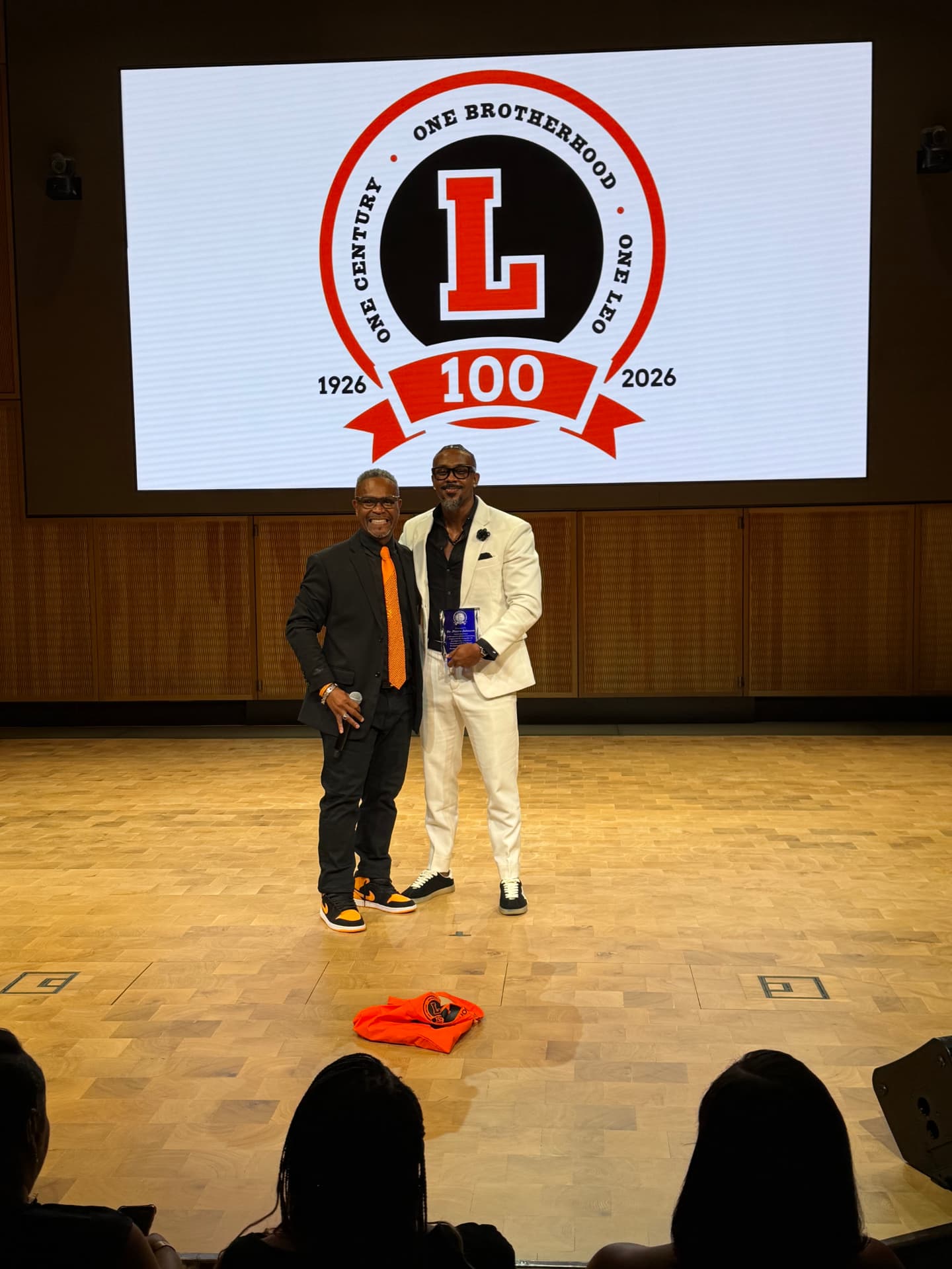 An honoree in a white suit holding his award beside the choir director on stage
