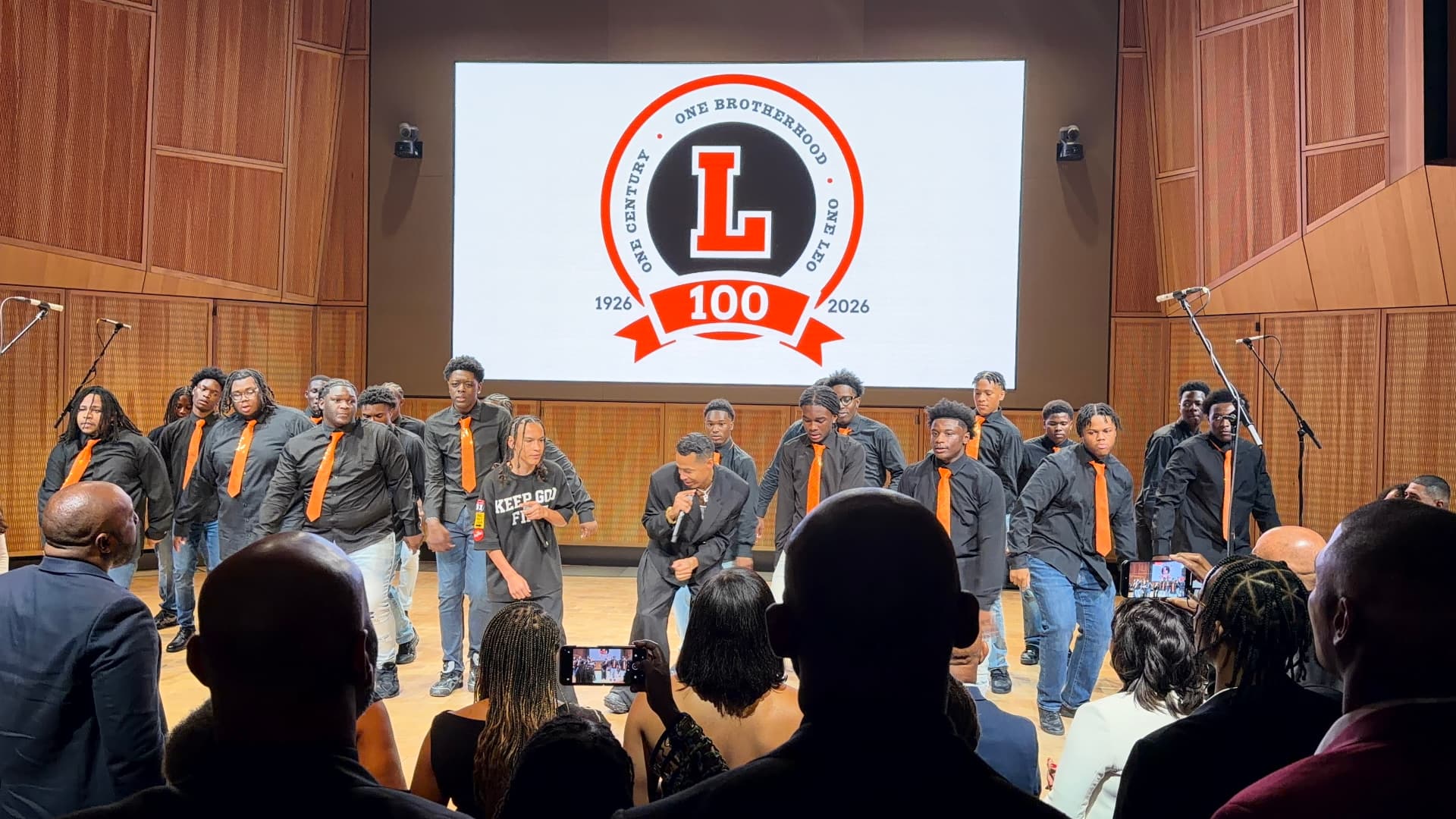 Guest vocalists and the choir moving together in front of the centennial crest