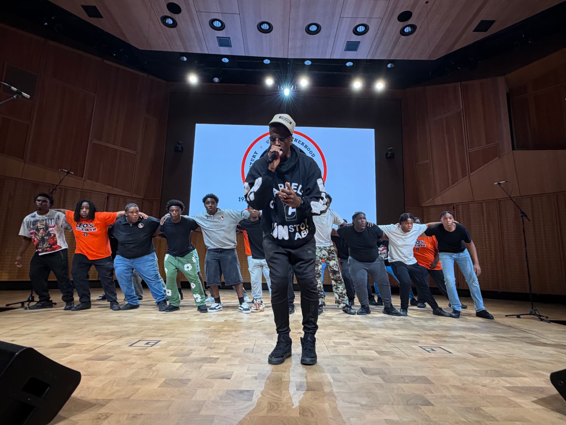 A guest vocalist rehearsing center stage as the choir links arms behind him