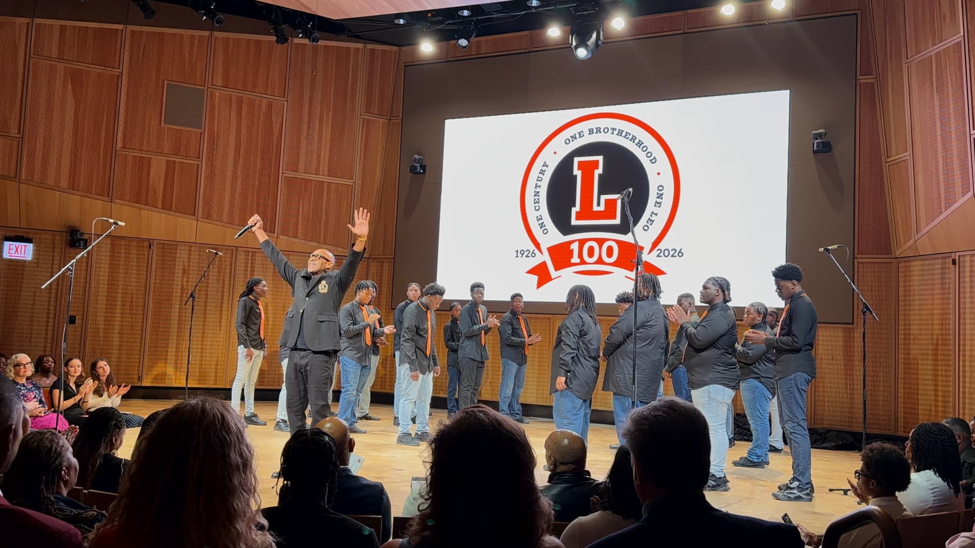 The director raising his arms in celebration as the choir applauds