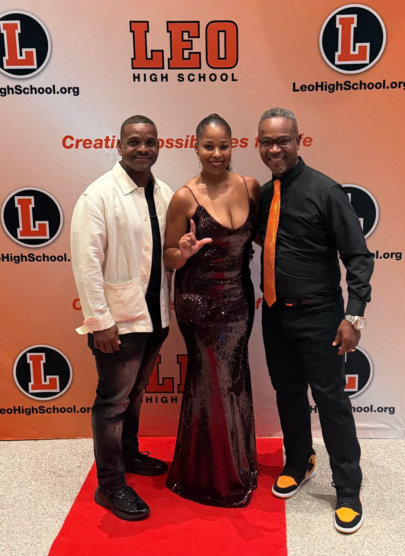 Three guests on the red carpet in front of the Leo High School backdrop, one throwing up the L