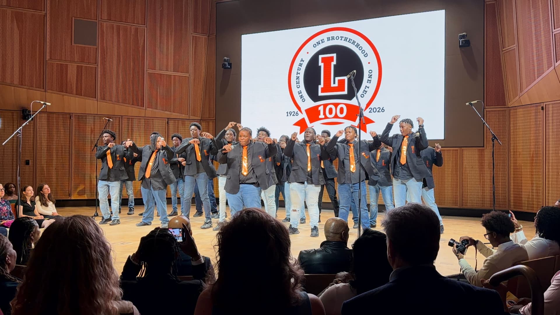 The choir moving together in choreography beneath the centennial crest