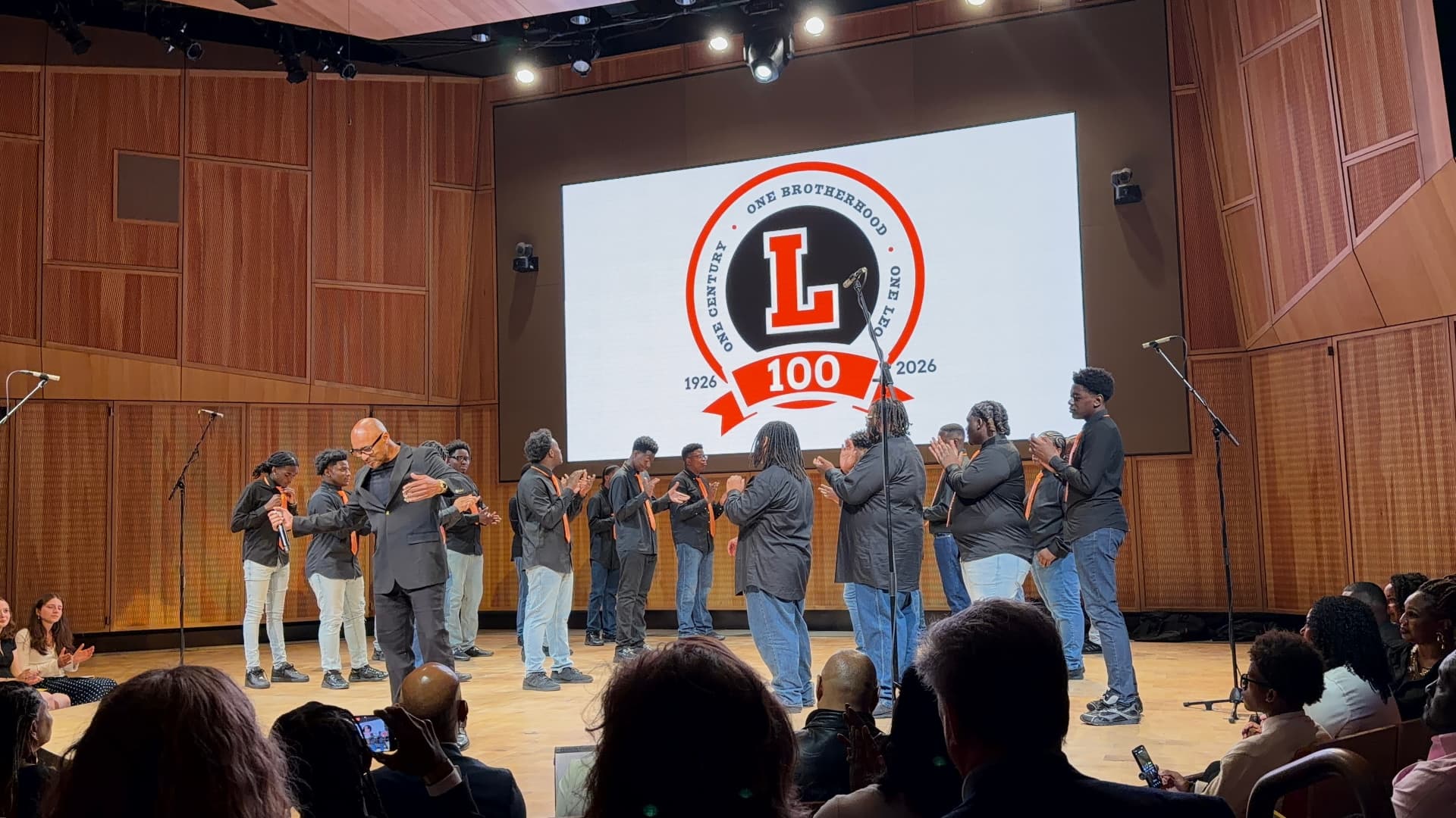 The director and choir clapping together on stage