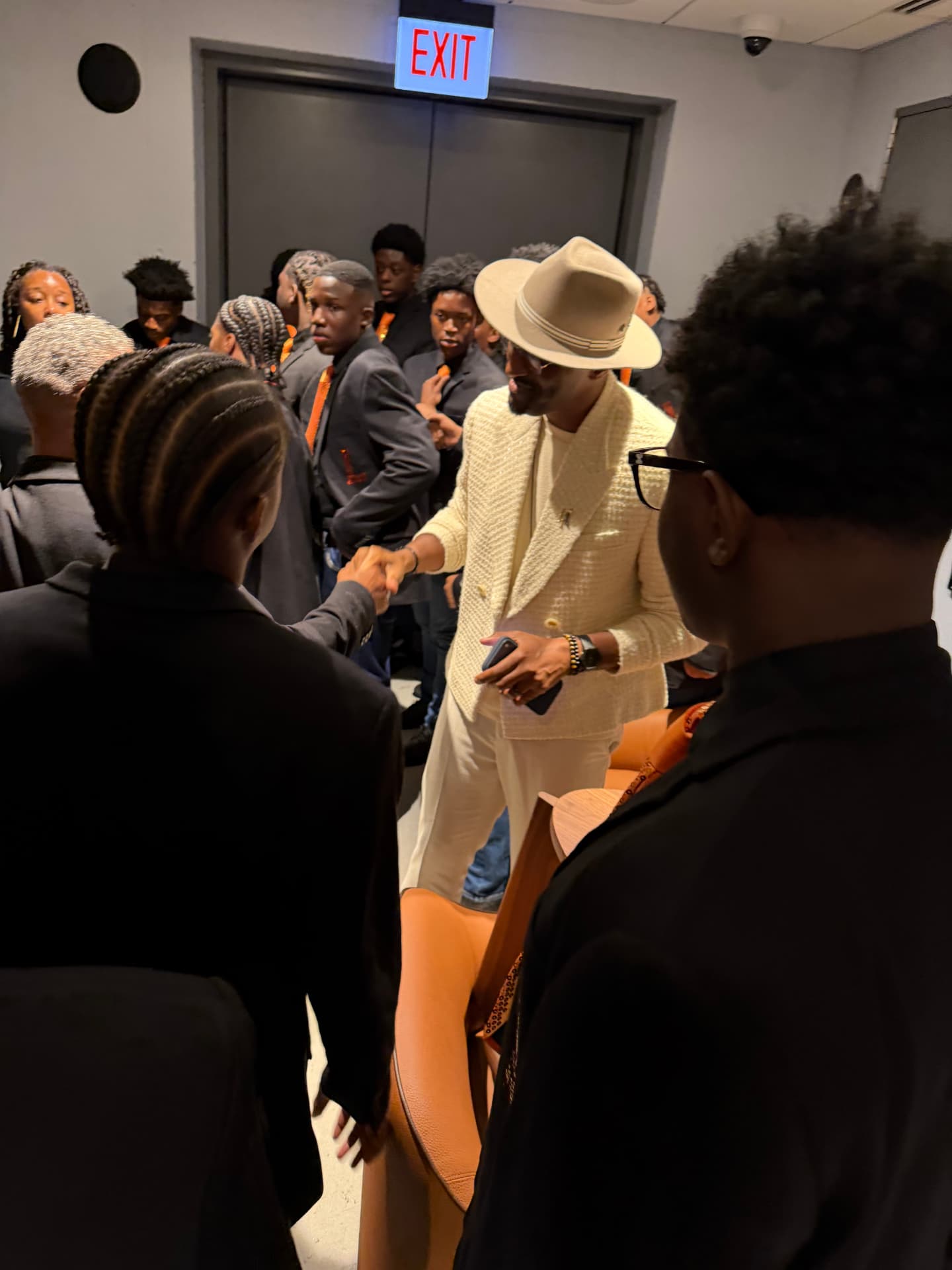 A guest artist in a cream suit and hat shaking hands with choir members backstage