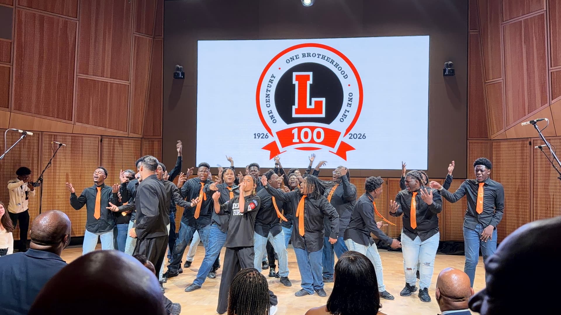 Choir members singing with hands raised around a young performer