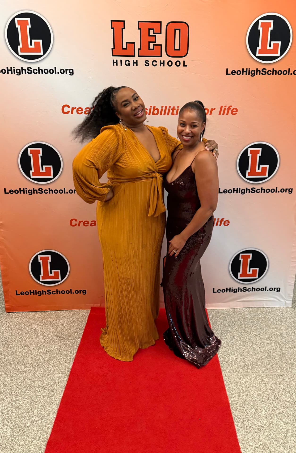 Two guests posing on the red carpet in front of the Leo High School backdrop