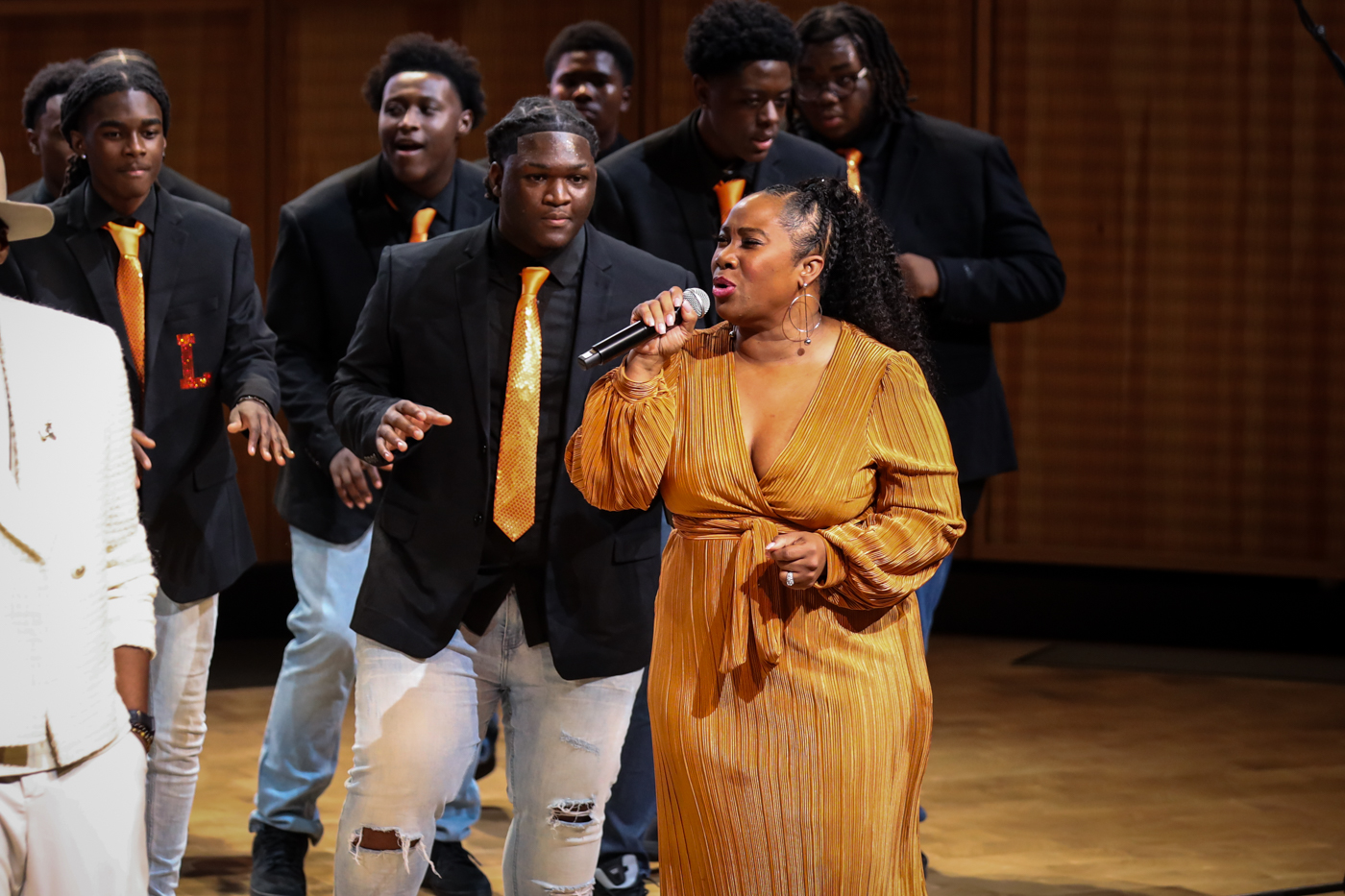 A vocalist in a gold dress singing with the choir behind her