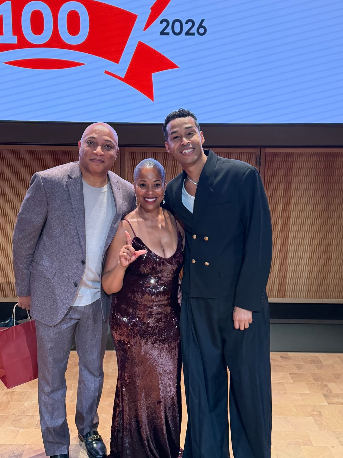 Three guests smiling on stage, one throwing up the L