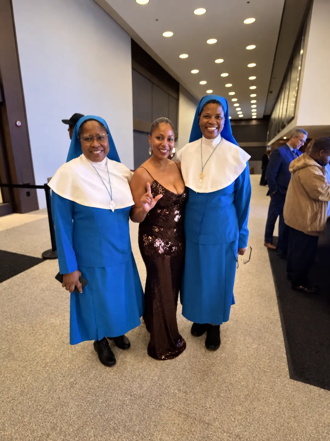 Two religious sisters in blue habits with a guest throwing up the L