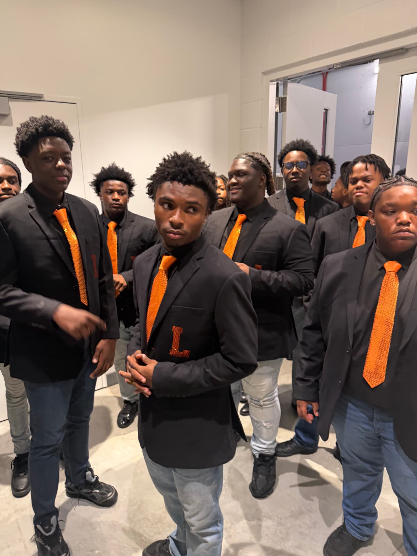 Choir members backstage in black blazers and orange sequined ties