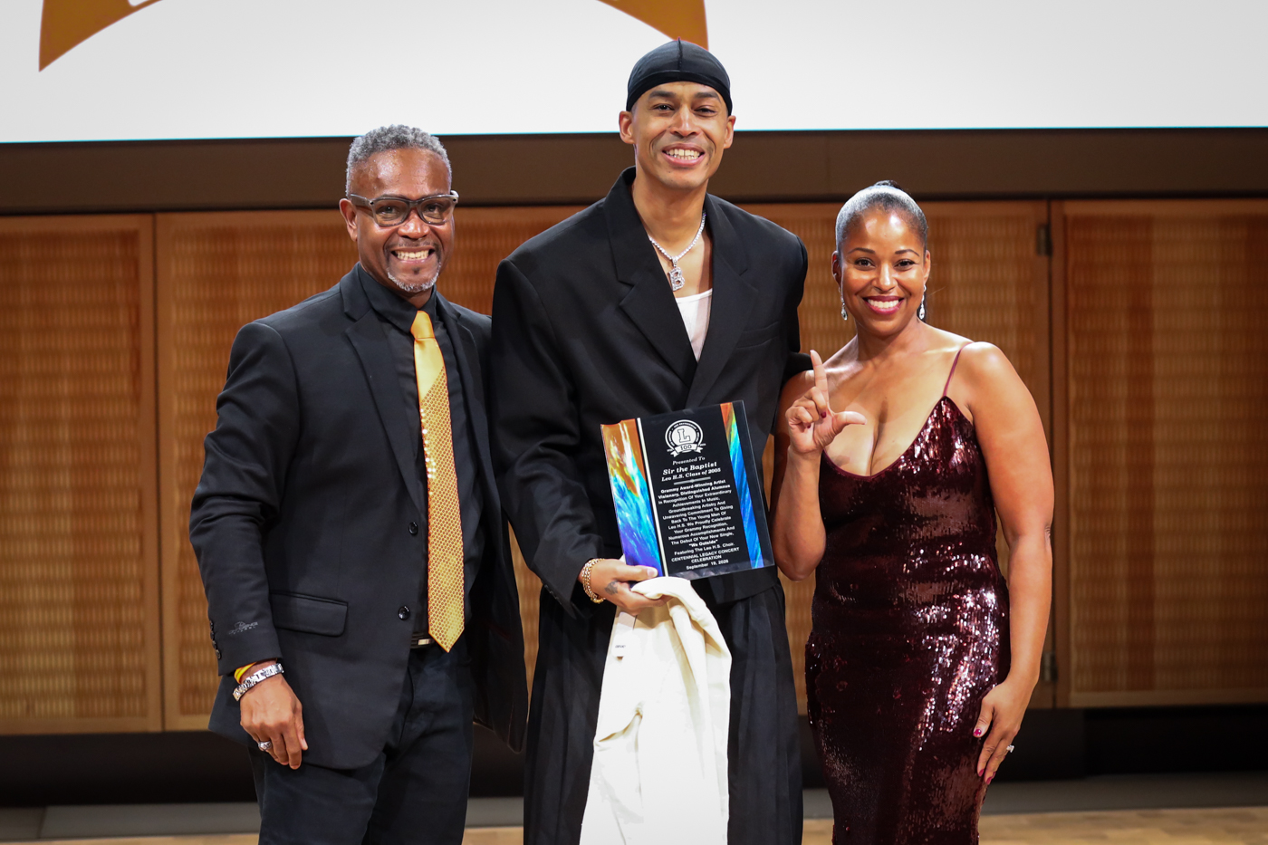 Sir the Baptist holding his alumni award between two presenters